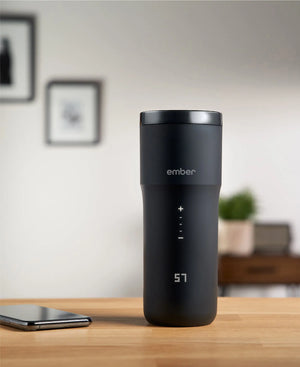 Electric Coffee Travel Mug juodas V2 - 355ml ant stalo su skaitmeniniu temperatūros rodmeniu modernioje vidaus aplinkoje.