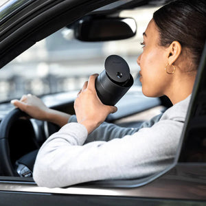 Asmuo geria kavą iš juodos termosinės puodelio su slankiojančiu dangteliu automobilyje, dalis „Take away“, „Fellow“, „EspressoGear“, viskas apie kavą.