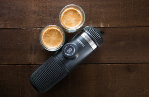Nešiojama espresso kavos aparatas su dviem espresso puodeliais ant medinio paviršiaus, iš nešiojamų kavos virimo aparatų ir baristos įrangos